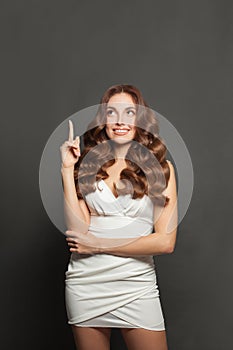 Young woman with curly shiny hair pointing up on gray studio wall background