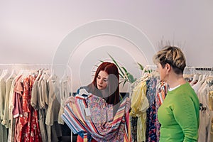 young woman customer advised to buy a dress, by a saleswoman expert in clothes, in a fashion shop. shopping concept.