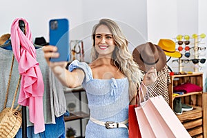 Young woman customer making selfie by smartphone holding shopping bags at clothing store