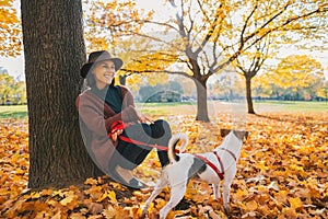 Young woman with cute dog sitting under tree in autumn park