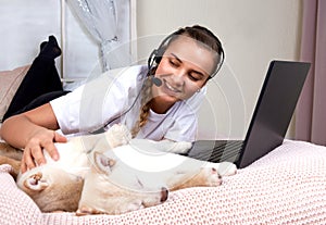 Young woman with cute puppy Shiba inu working at home during quarantine with laptop in bed