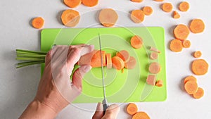Young woman cuts fresh young carrots with knife on cutting board top view. Cutting vegetables close-up, cooking at home
