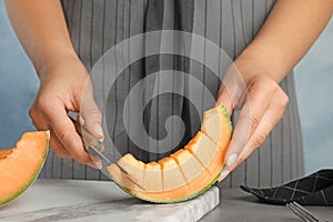 Young woman cutting cantaloupe melon slice at table