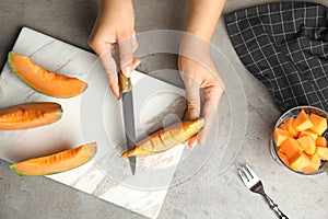 Young woman cutting cantaloupe melon slice at table