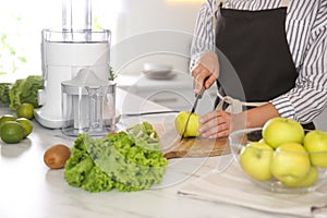 Young woman cutting fresh apple for juice at table in kitchen, closeup