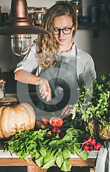 Young woman cutting fresh herbs and vegetables for cooking