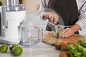 Young woman cutting fresh kiwi for juice at table in kitchen, closeup