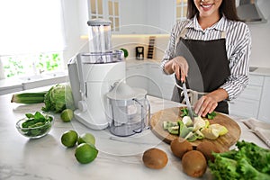 Young woman cutting fresh spinach for juice at table in kitchen, closeup