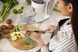 Young woman cutting fresh spinach for juice at table in kitchen