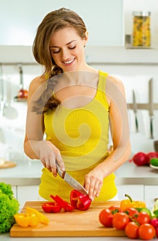 Young woman cutting fresh vegetables in kitchen