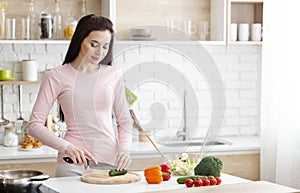 Young woman cutting fresh vegetables in kitchen