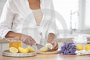 Young woman cutting lemon on wooden board. Preparation of fresh llemonade.