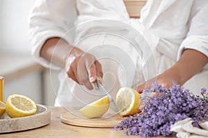 Young woman cutting lemon on wooden board. Preparation of fresh llemonade.