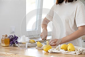 Young woman cutting lemon on wooden board. Preparation of fresh llemonade.