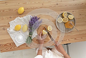 Young woman cutting lemon on wooden board. Preparation of fresh llemonade.