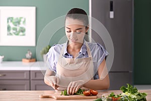 Young woman cutting parsley for salad in kitchen