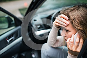 Young woman in the damaged car after a car accident, making a phone call.