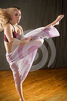 Young woman dancer dramatically kicking in lavender skirt.