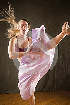 Young woman dancer dramatically kicking in lavender skirt.