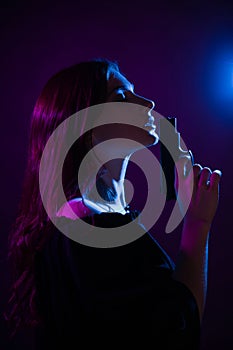 A young woman in the dark in a club holds a gun. Party girl in blue and pink light