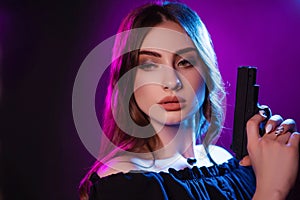A young woman in the dark in a club holds a gun. Party girl in blue and pink light