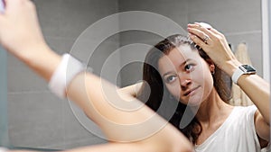 Young woman with dark curly hair doing self hair scalp massage with scalp massager or hair brush for hair growth