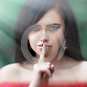 Young woman with dark long hair saying shh with forefinger on lips. silence gesture