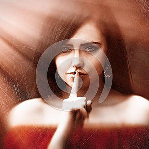 Young woman with dark long hair saying shh with forefinger on lips. silence gesture