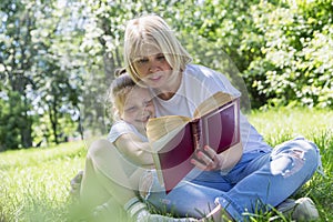 Young woman with a daughter are reading a book in a park on a sunny summer day. Love and tenderness