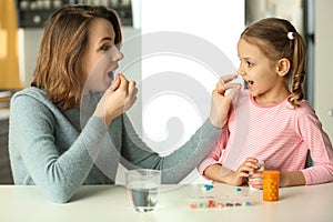 Young woman and daughter taking pills at table