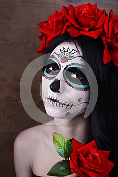 Day of the dead. Halloween. Young woman in day of the dead mask skull face art and rose. Dark background.