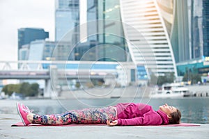 Young woman in Dead Body pose against the skyscraper