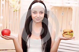 A young woman decides between hamburger and apple. Healthy Lifestyle