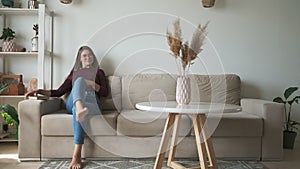 Young woman decorates home interior and sits on the sofa to relax and read book