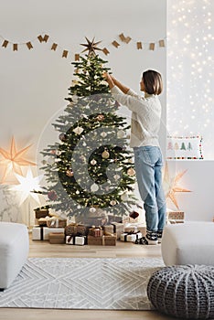 Young woman decorating Christmas tree at home, winter holiday and xmas time concept