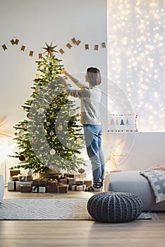 Young woman decorating Christmas tree at home, winter holiday and xmas time concept