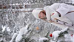 Young woman decorating fir tree with red bauble in snowy winter forest
