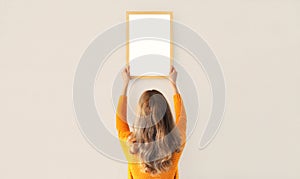 Young woman decorating interior, hanging blank a photo frame mockup on white wall in a new house