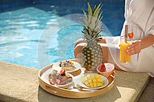 Young woman with delicious breakfast on tray near swimming pool, closeup