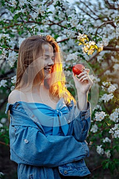 Young woman in denim jacket smiling while looking at an apple.
