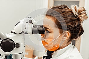 Young woman dentist doctor looks through a professional microscope in a dental clinic. A doctor in a disposable medical