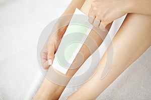 Young woman depilating her leg with wax stripe at home