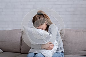 Young woman with depression hugging pillow and crying on sofa at home
