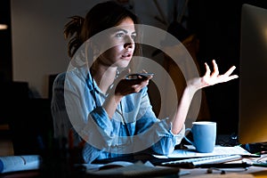 Young woman designer sitting in office working using mobile phone at night.