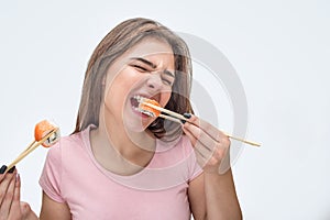 Young woman devour pieces of sushi. She bite piece. Model hold them with chopsticks. Isolated on grey background.