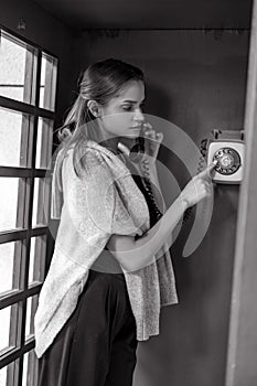 Young woman dials phone number in payphone booth