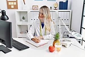 Young woman dietician writing on document at clinic