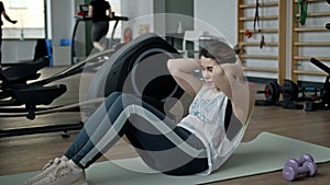 Young woman with difficulty shakes the press, lying on a mat in a fitness room.