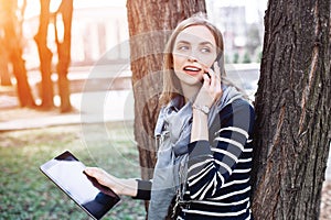 Young woman with digital tablet in hand talking on mobile phone with boyfriend before a meeting with it. Attractive girl