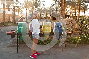 Young woman disposing of paper, throwing it into a yellow vase in park. Pretty female in casual wear and sneakers care